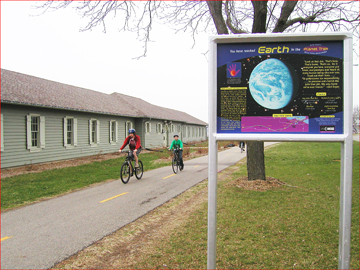Two cyclists bike alongside the Planet Trek Earth sign.