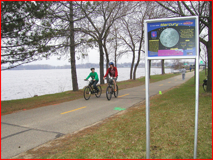 Two cyclists bike alongside the Planet Trek Mercury sign.