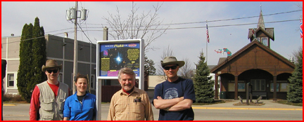 Four people stand at the Pluto sign on the Planet Trek path, smiling.